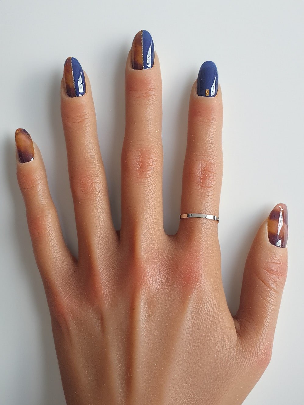 Main avec vernis auto-adhésifs bleu profond et accents marron, dicrètes lignes dorées.