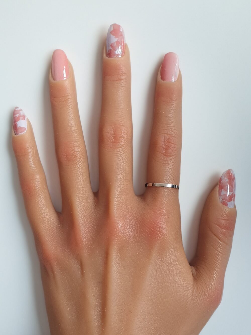 Main avec des autocollants pour les ongles à motifs floraux sur fond nude.