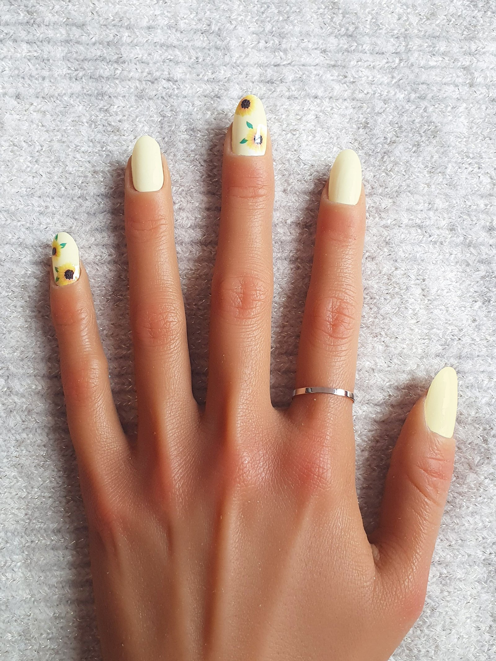 Main avec des vernis à ongles autocollants jaunes et motifs de tournesols