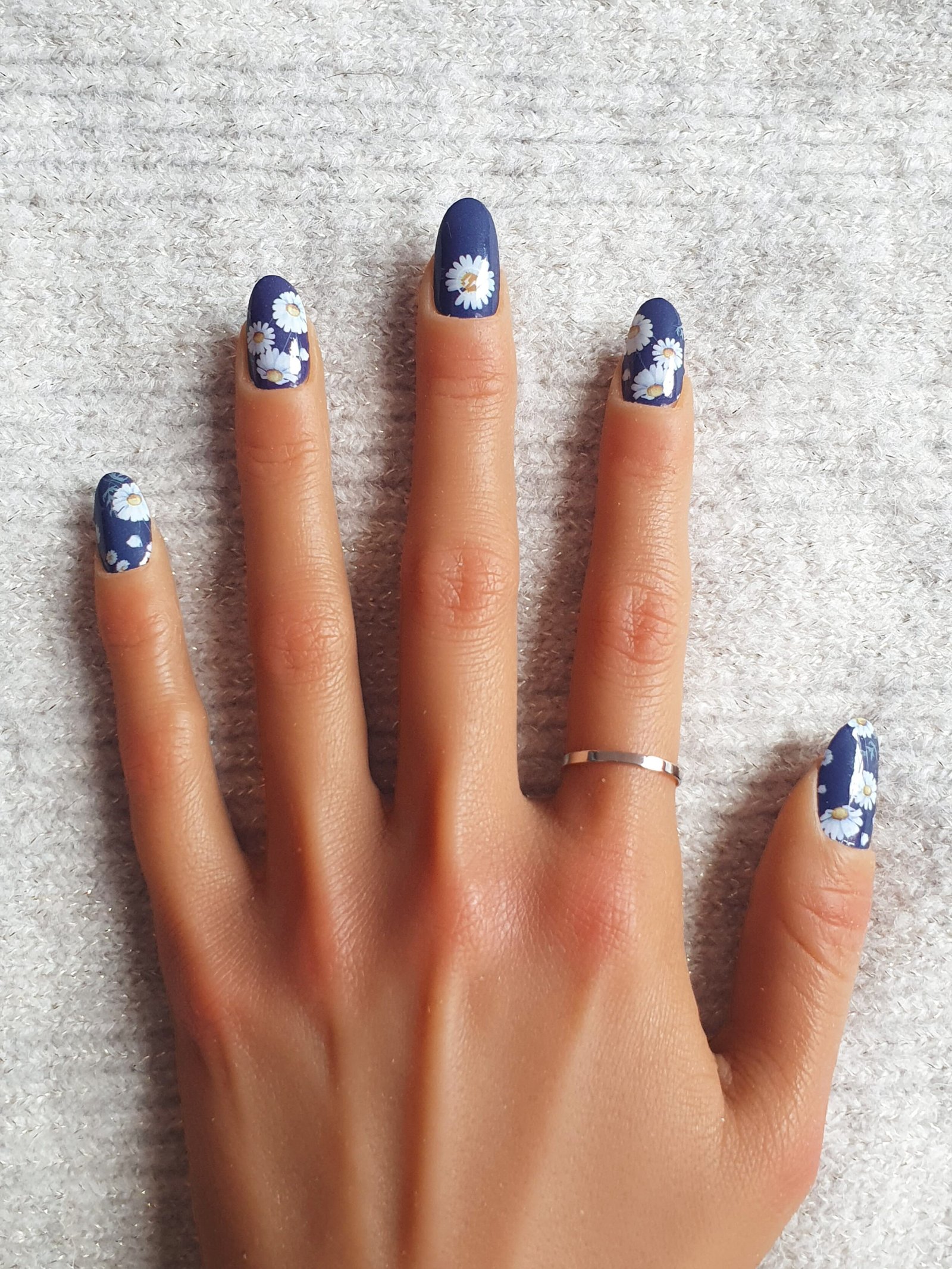 Alternative au gel UV pour ongles avec une manucure avec stickers ongles fleurs blanches sur fond bleu marine.