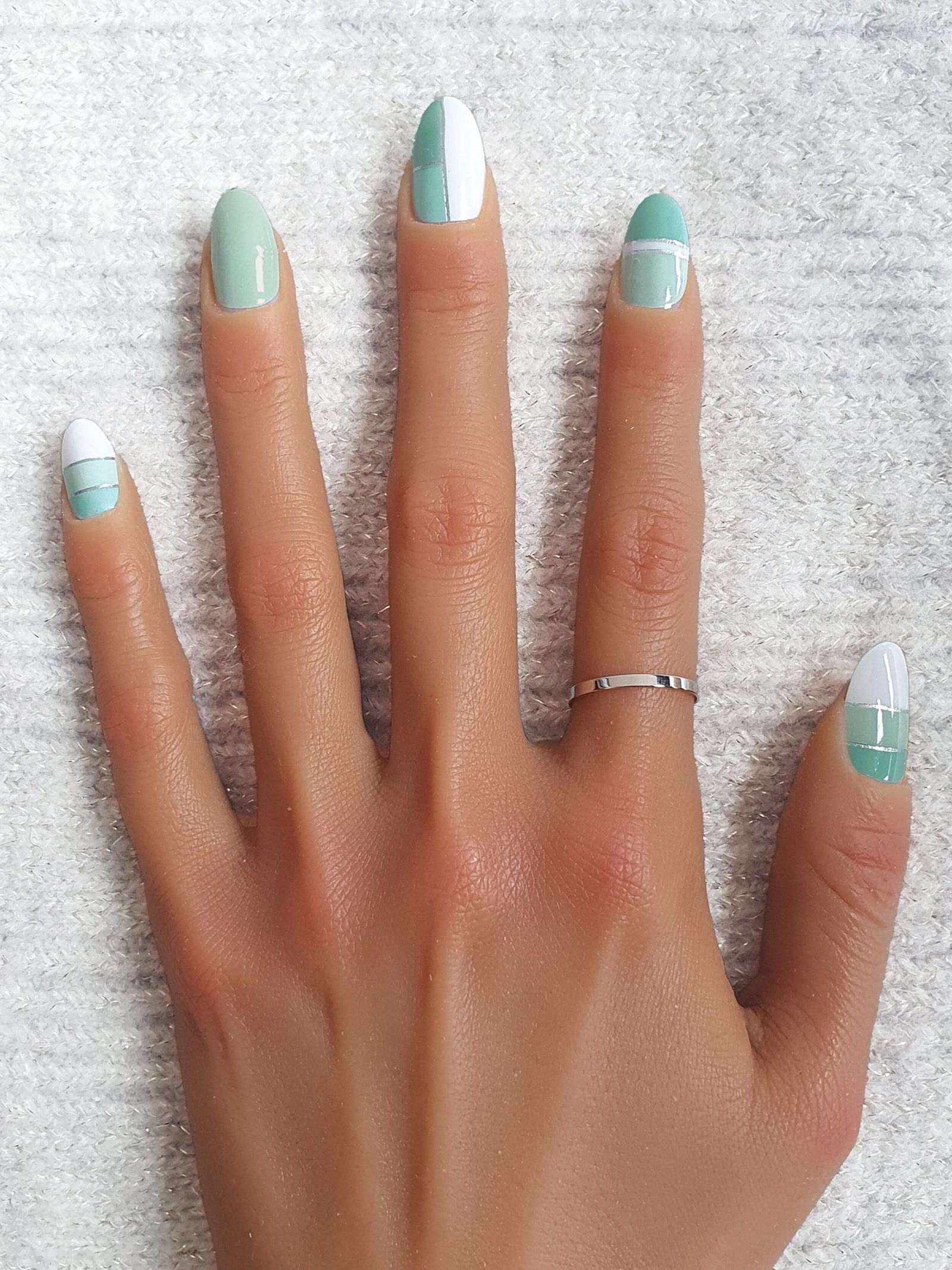 Main avec des décorations pour les ongles géométriques vert menthe et blanc.