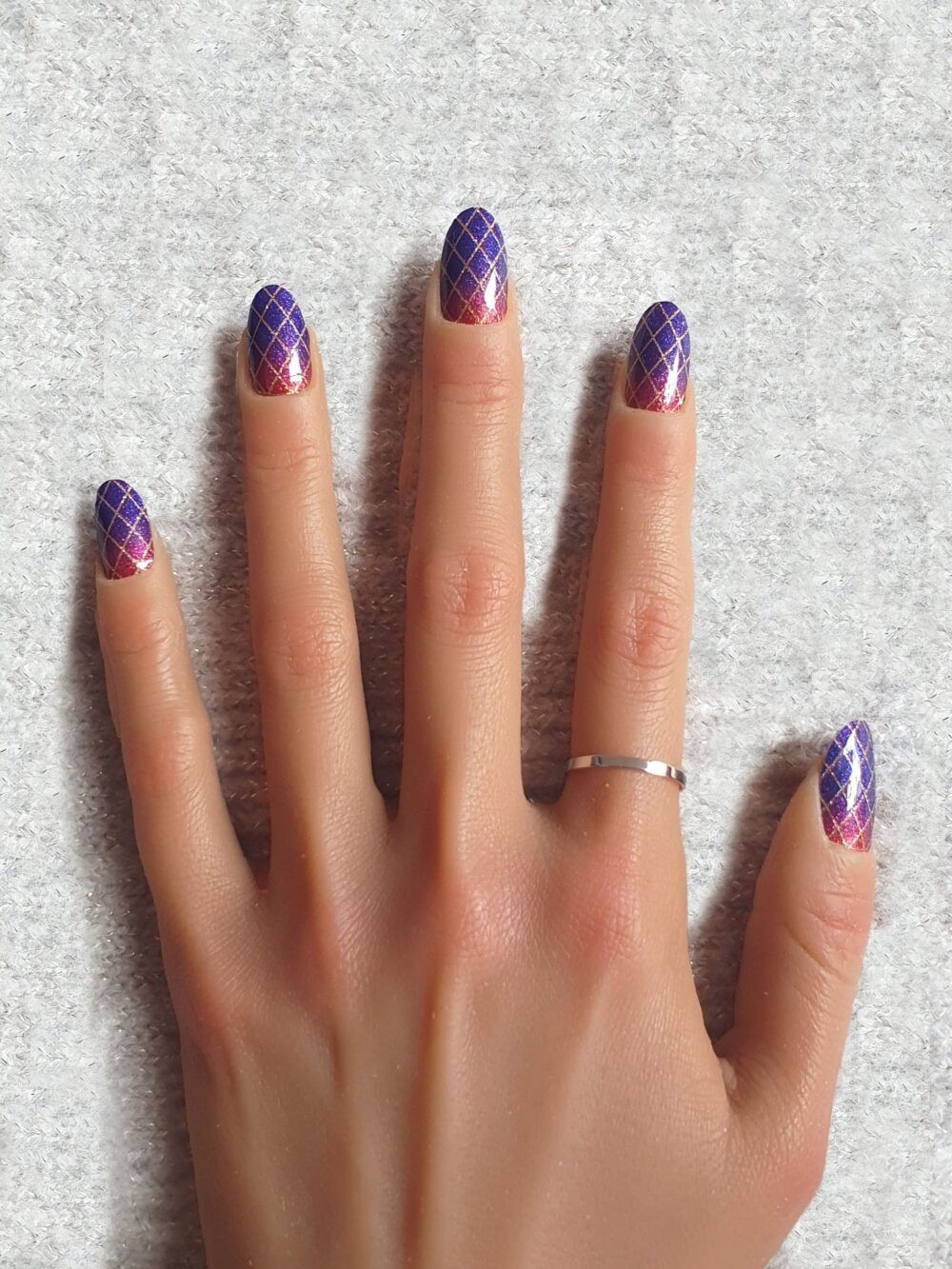 Manucure avec stickers ongles pailletés, couleurs violet et rose foncé, et motif géométrique doré.